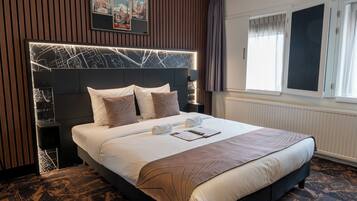 Une chambre d’hôtel avec un grand lit, une tête de lit ornée d’un motif représentant une carte, une table de chevet, une fenêtre avec des rideaux et un téléviseur fixé au mur.
