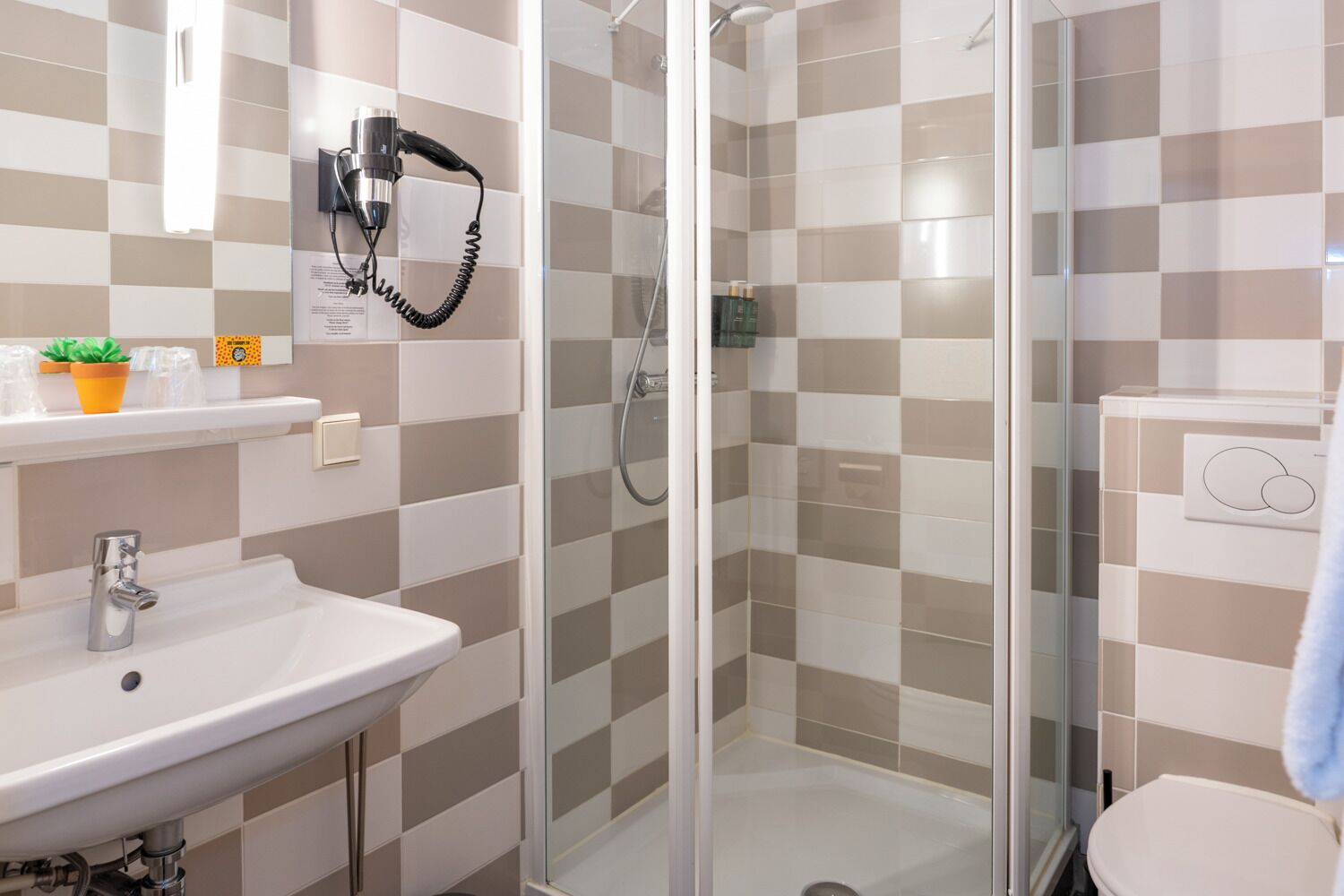 A bathroom with a sink, a hairdryer mounted on the wall, a shower with glass doors, and a toilet.