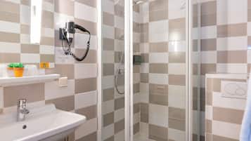 Un baño con lavamanos, secador de pelo montado en la pared, ducha con puertas de vidrio y un inodoro.