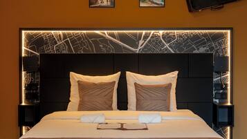 Habitación de hotel con una cama grande, dos mesitas de noche, un cabecero con diseño de paisaje urbano y un televisor de pantalla plana montado en la pared.
