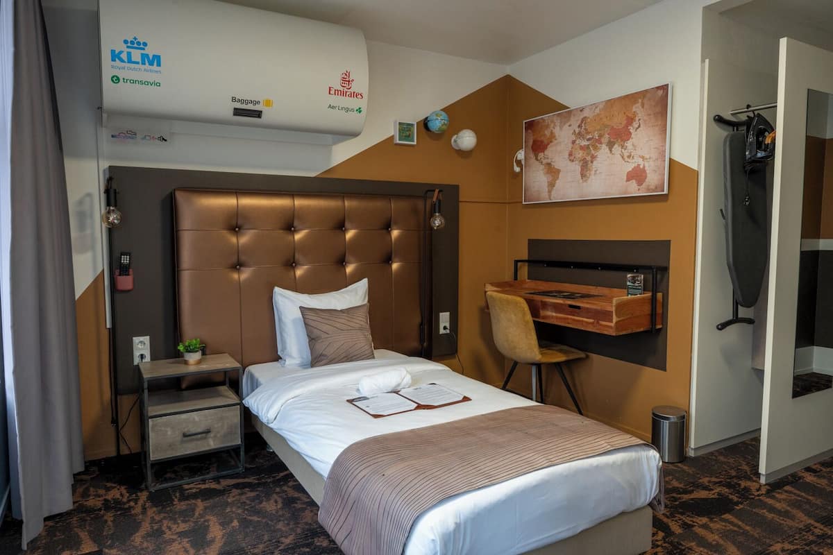 A hotel room with a large bed, a desk, a chair, a map on the wall, and an air conditioning unit.
