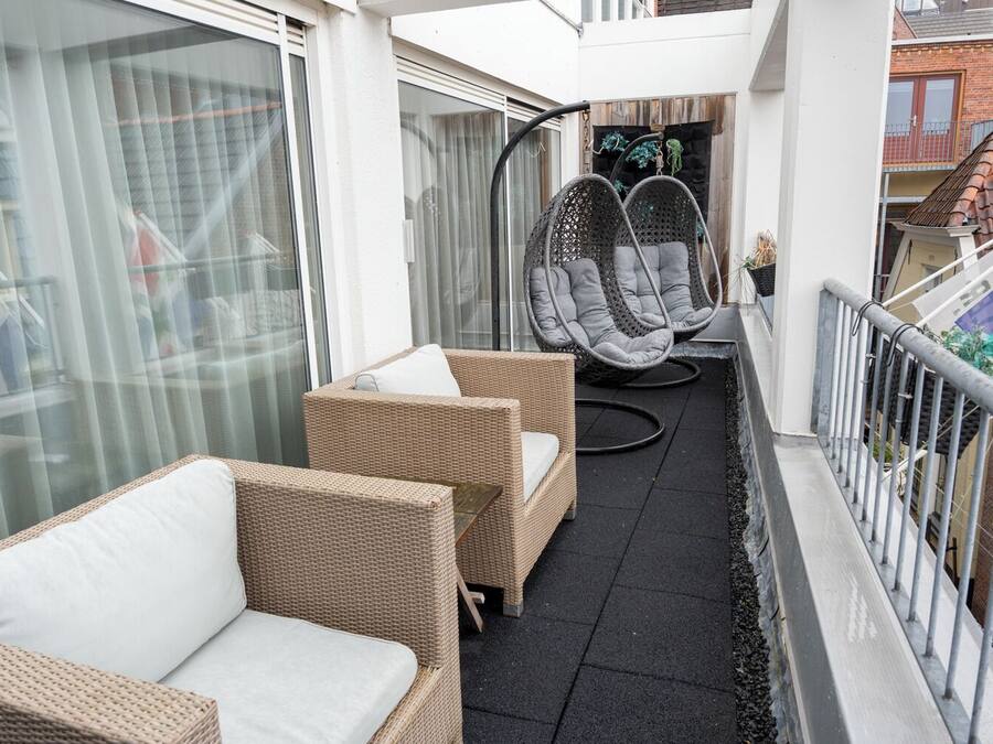 A balcony with wicker furniture, a hanging chair, and a view of the city.