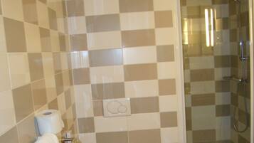 A bathroom with a checkered tile wall, a toilet, a towel rack, and a glass-enclosed shower area.