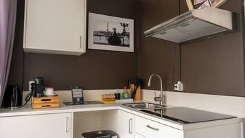 A compact kitchenette with a sink, a coffee maker, a trash bin, and a framed photo on the wall.