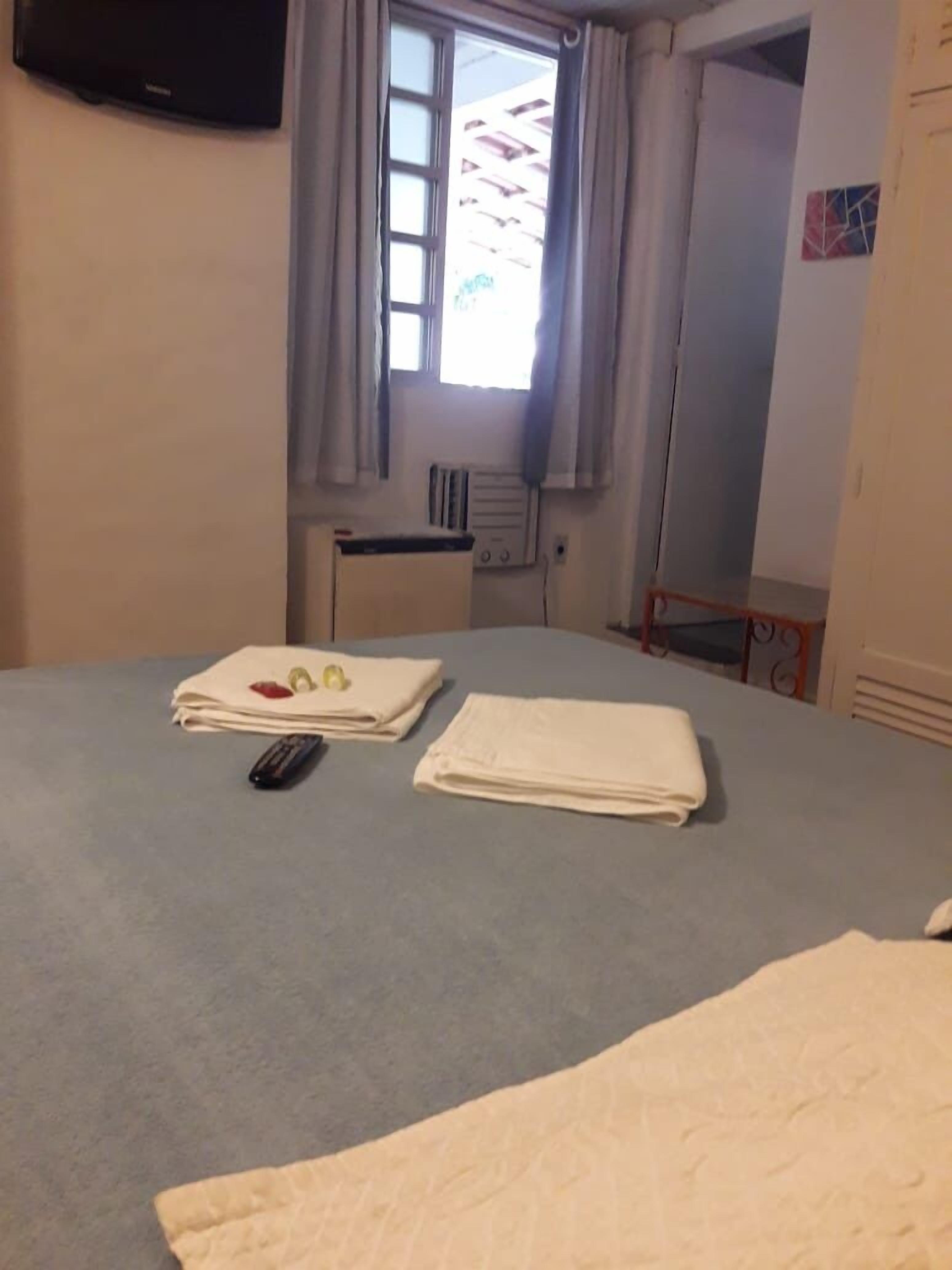 Habitación de hotel con una cama, un control remoto y toallas dobladas con cuidado sobre la cama.