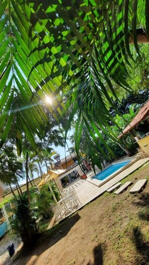 A pool area with a clear view of the pool, surrounded by lush greenery and a wooden deck. - Buzios Colinas Homestay (Búzios)