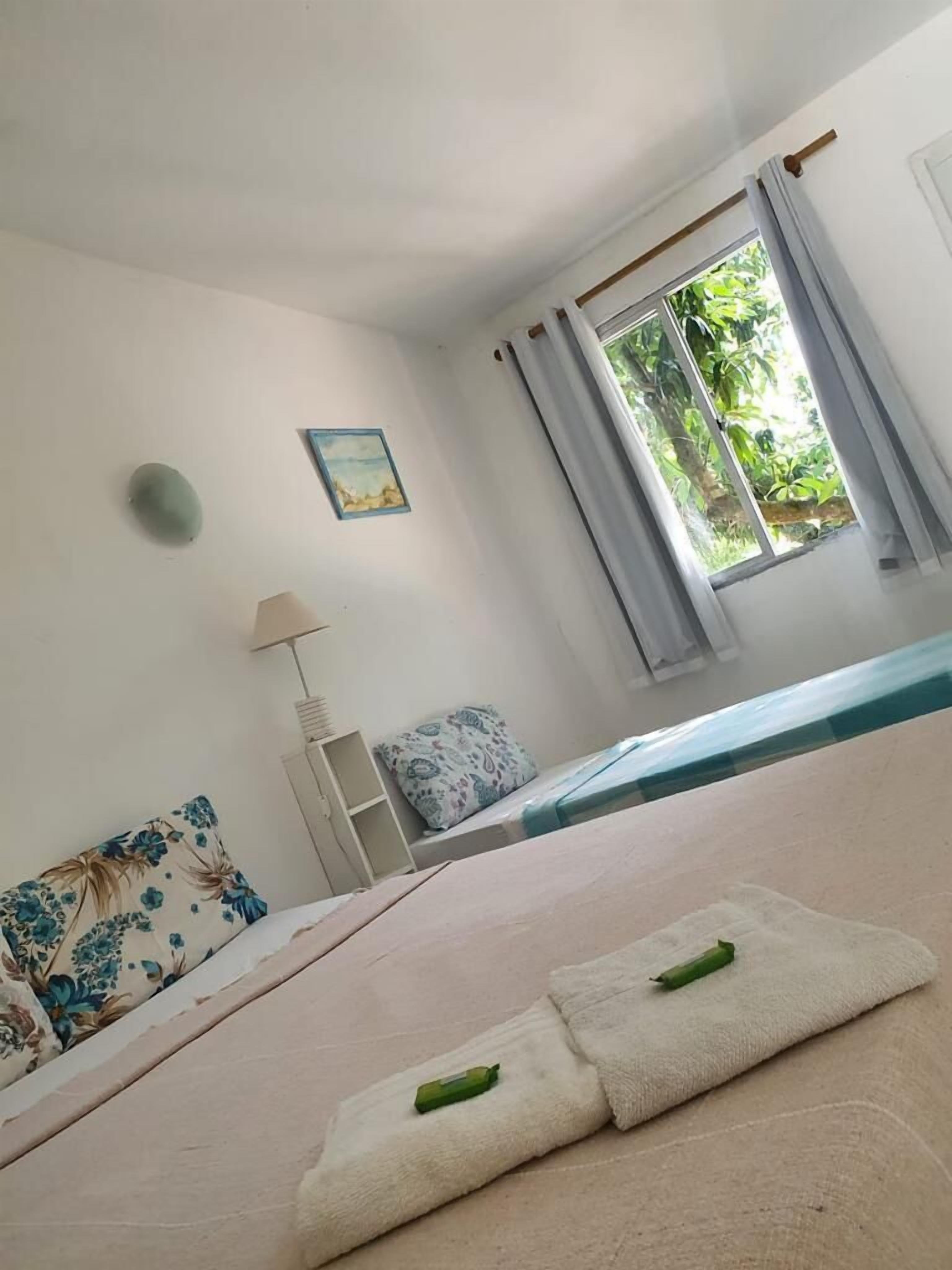 Un dormitorio con cama, mesita de noche, lámpara, ventana con cortinas e imagen colgada en la pared.