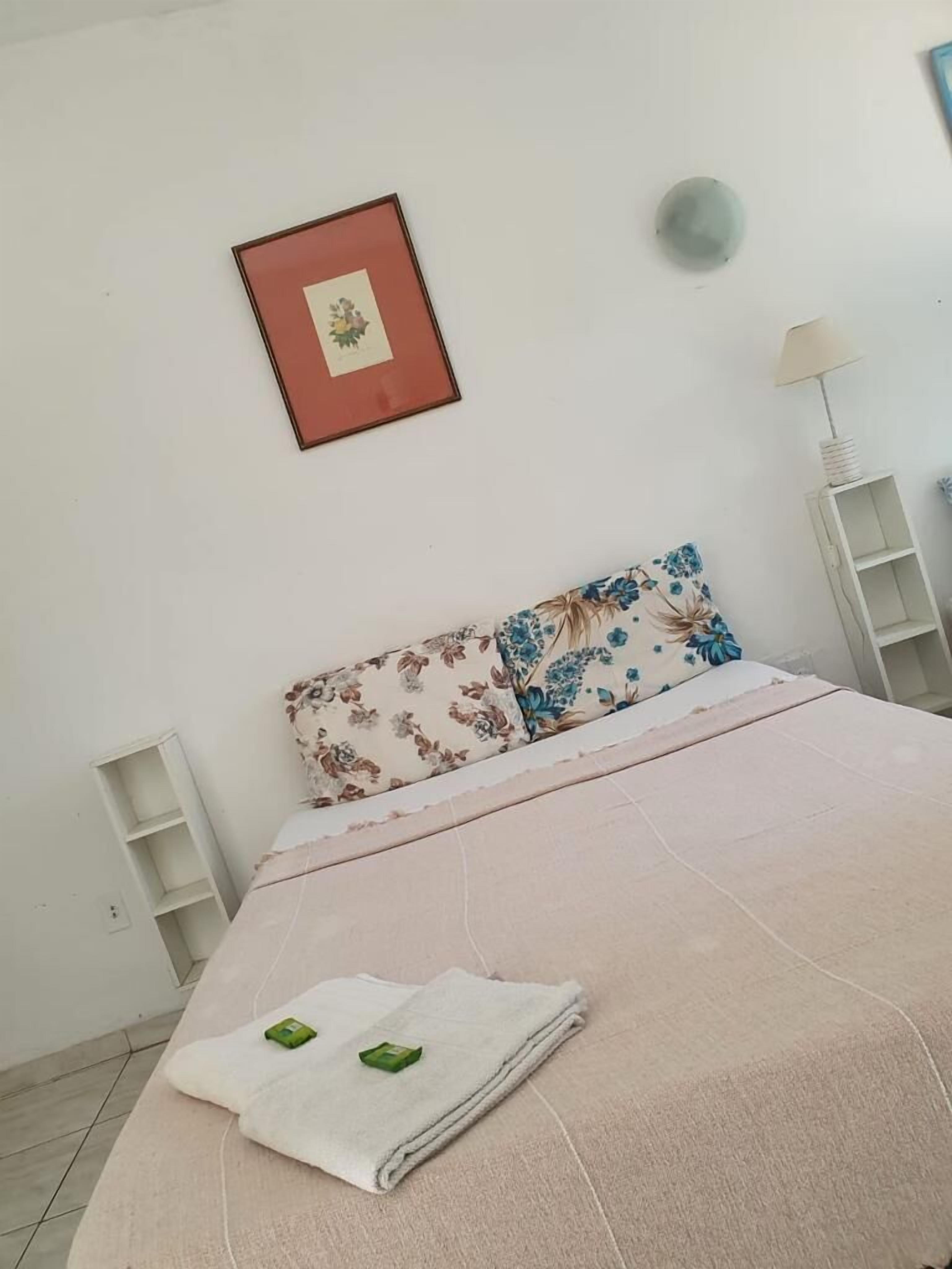 Un llit ben fet amb una almofada floral, una petita taula de nit, un quadre penjat a la paret i una làmpada de peu.