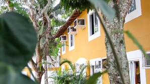 Un bâtiment jaune aux ornements blancs, entouré d’arbres et de plantes.
