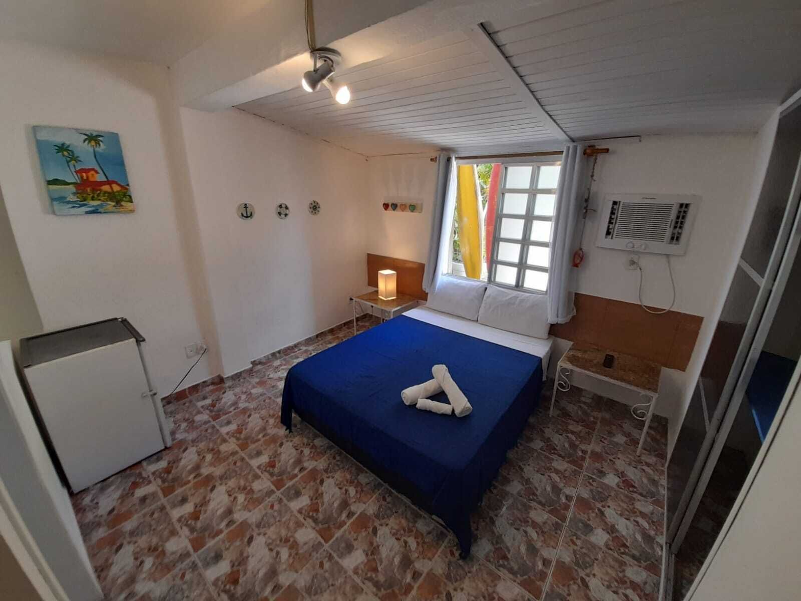 A hotel room with a bed, a nightstand, a lamp, a window with curtains, and a painting on the wall.