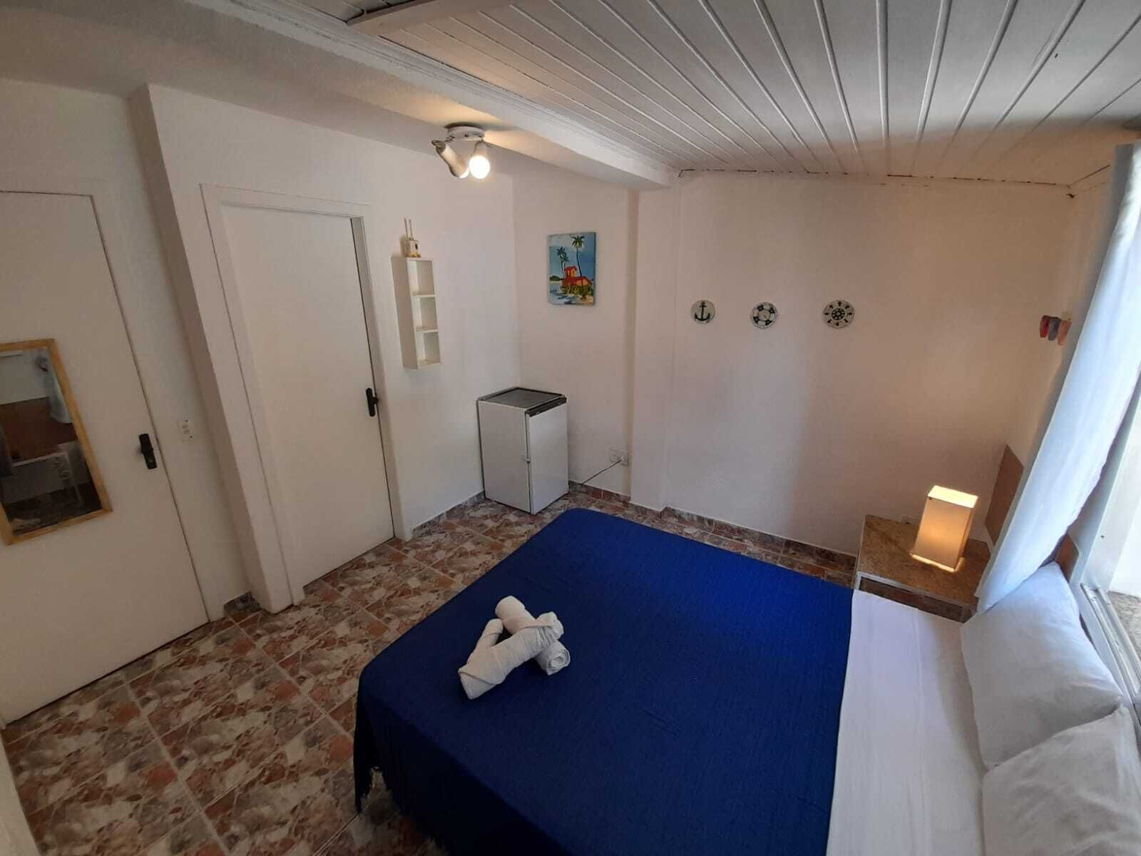 Um quarto com cama, uma pequena escrivaninha, prateleira na parede e iluminação no teto.