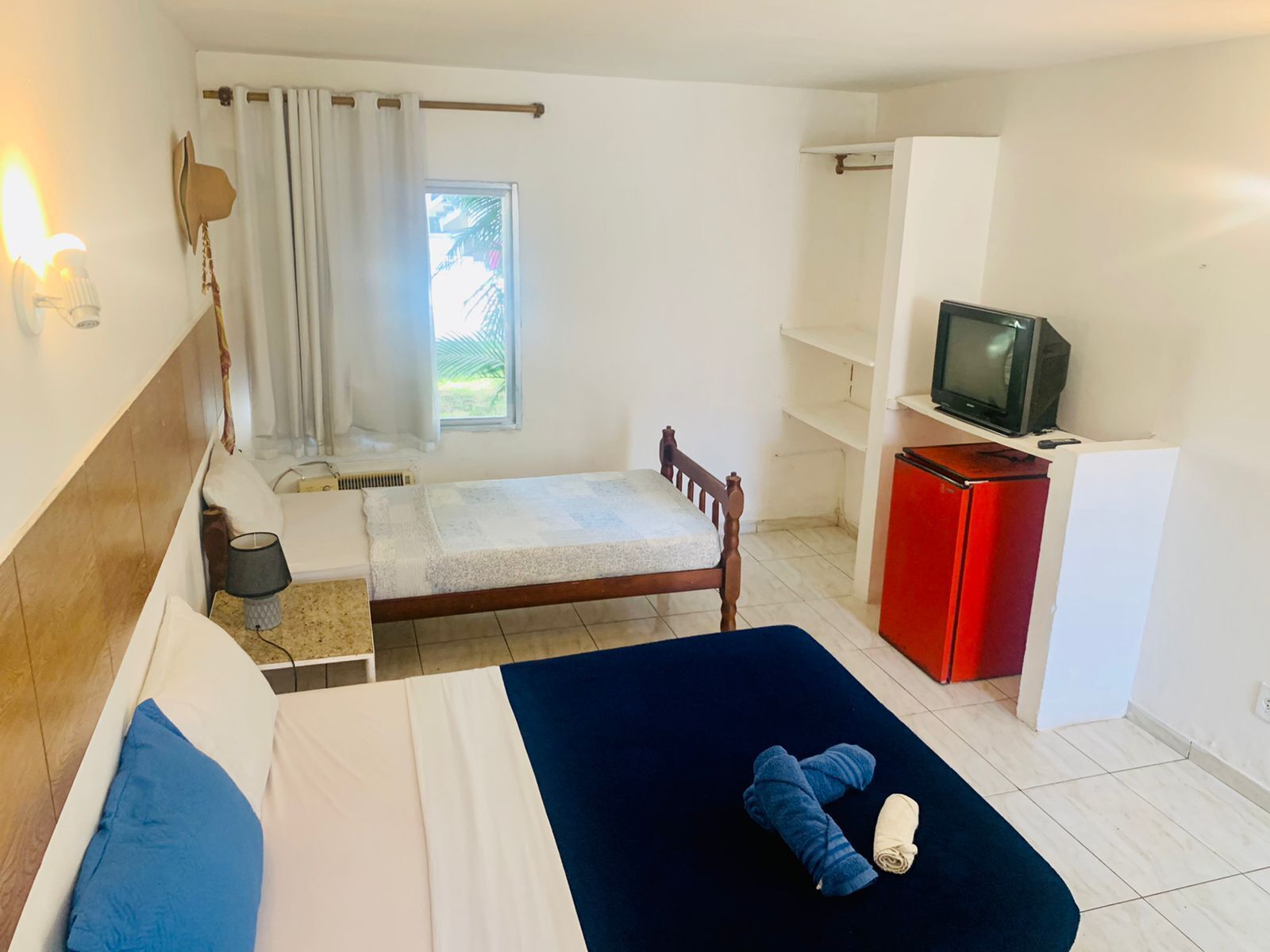A bedroom with a bed, a TV, a red cabinet, and a window with curtains.