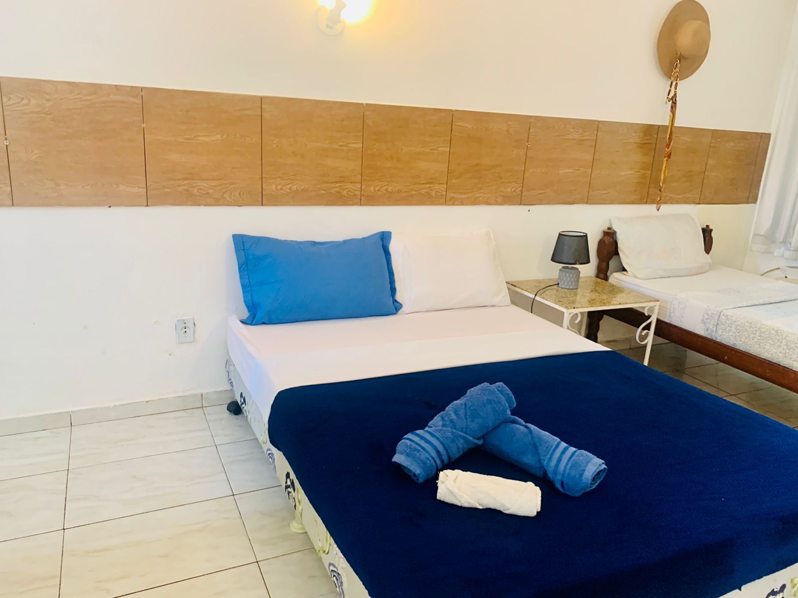 A hotel room with a bed, a nightstand, a lamp, and a hat hanging on the wall.