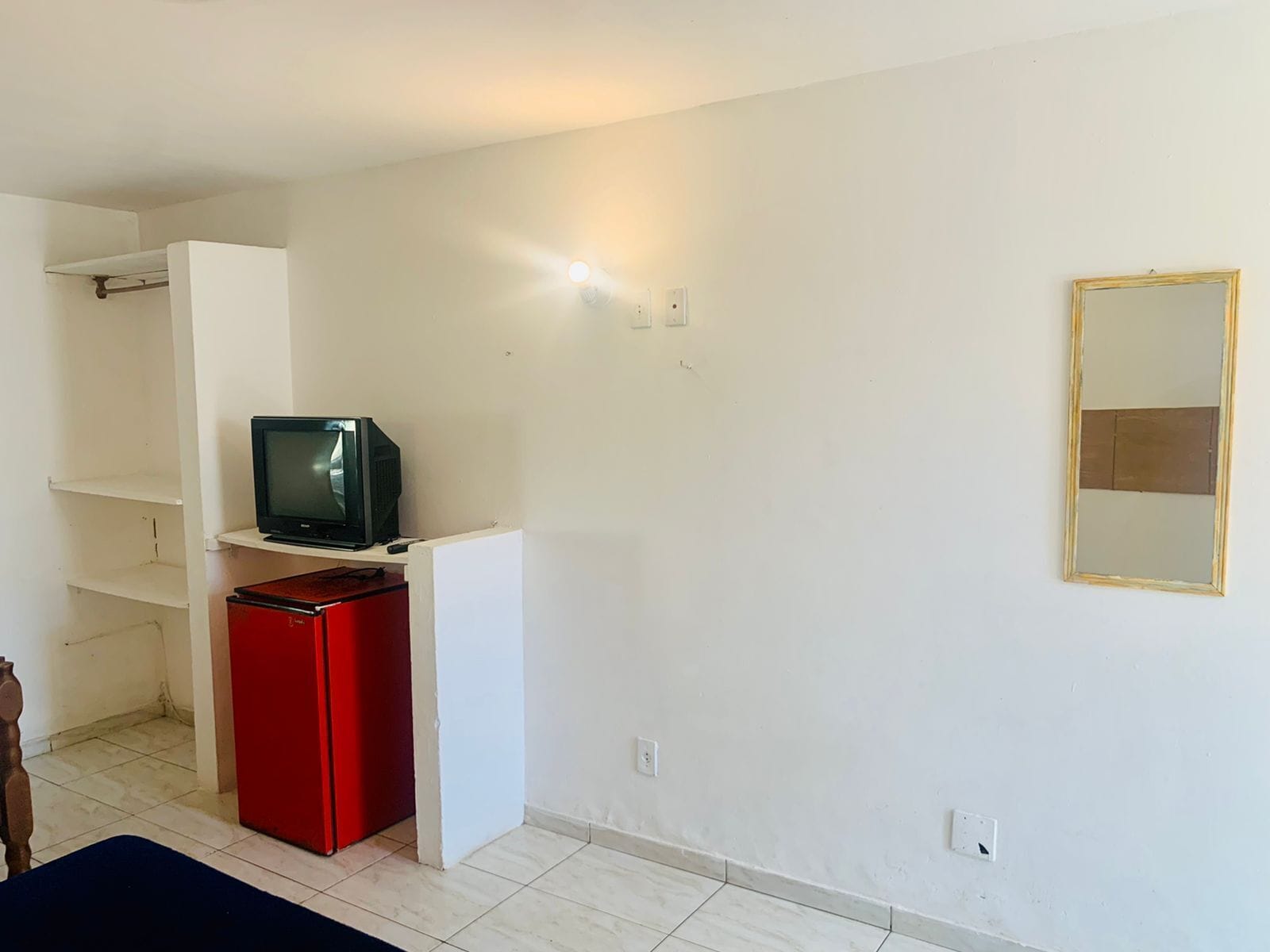 A room with a television on a white stand, a red cabinet, and a mirror on the wall.
