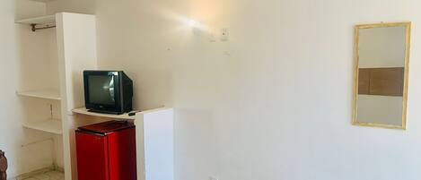 A room with a television on a white stand, a red cabinet, and a mirror on the wall.