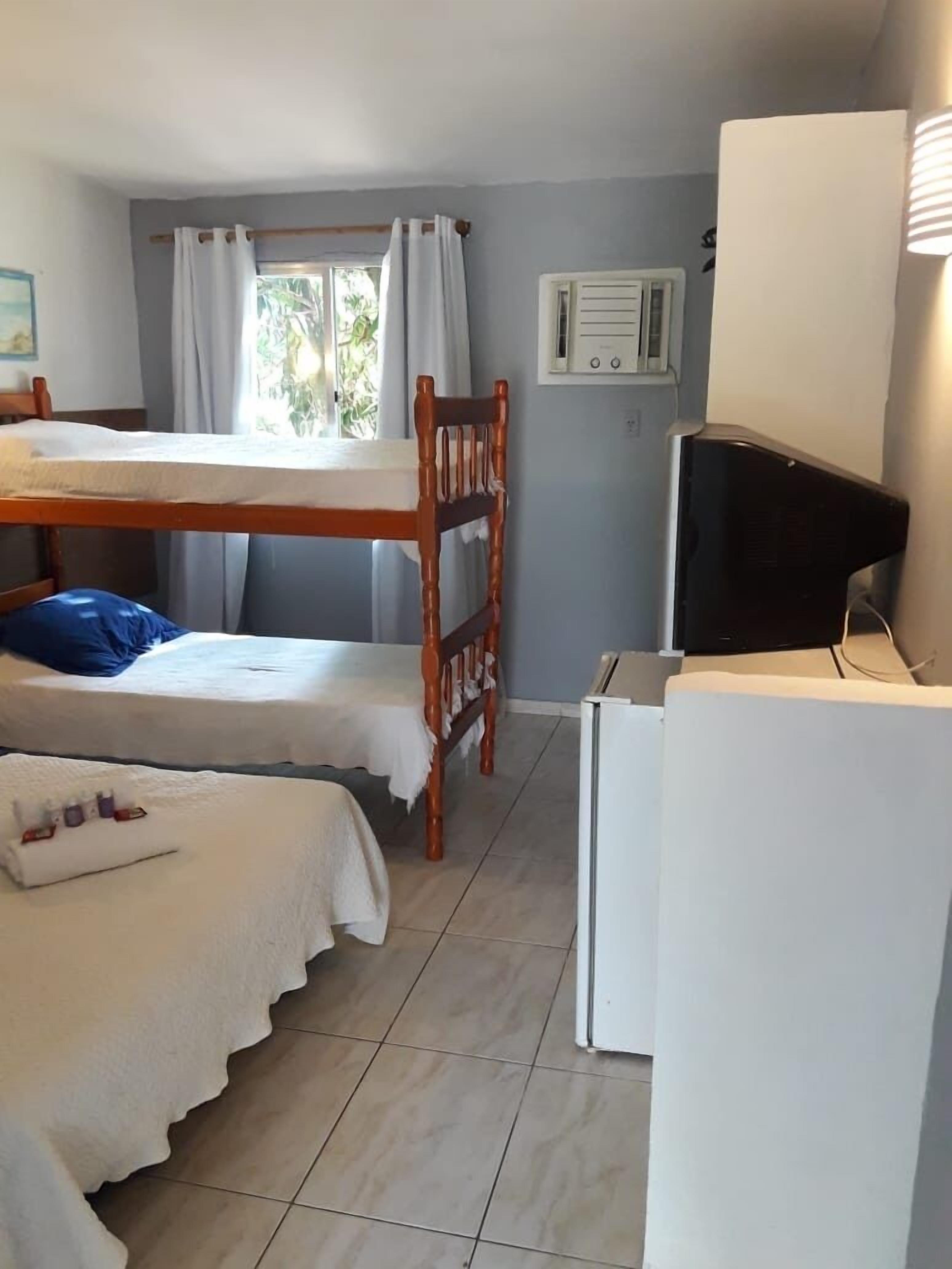 Une chambre de dortoir équipée de lits superposés, d’un bureau, d’une chaise, d’un téléviseur et d’une fenêtre avec des rideaux.