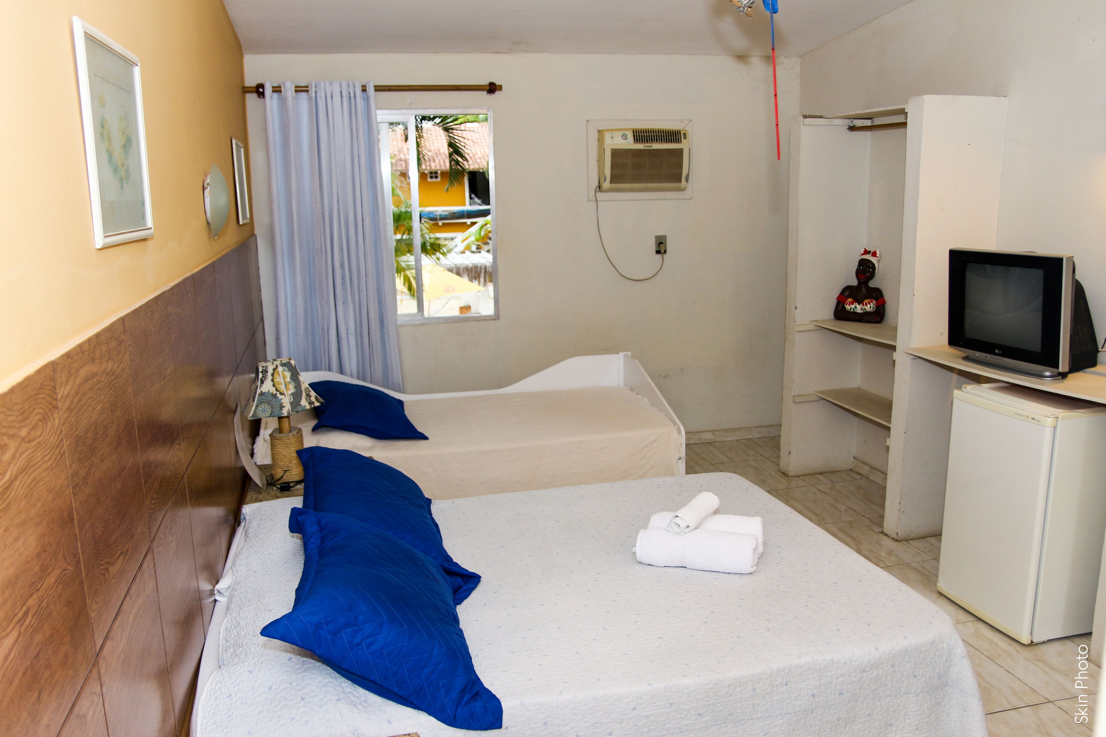 Camera d'albergo con due letti, TV, piccolo frigorifero e finestra vista palma.