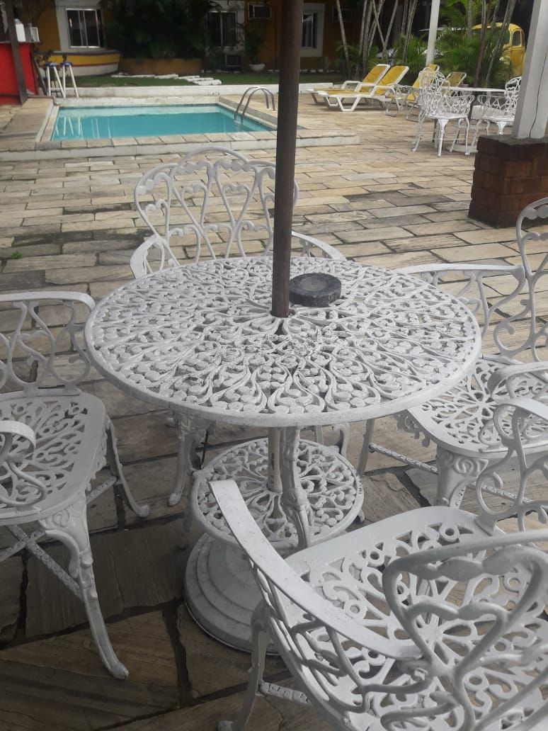 A poolside area with a round metal table and chairs, a small pool, and a yellow vehicle in the background.