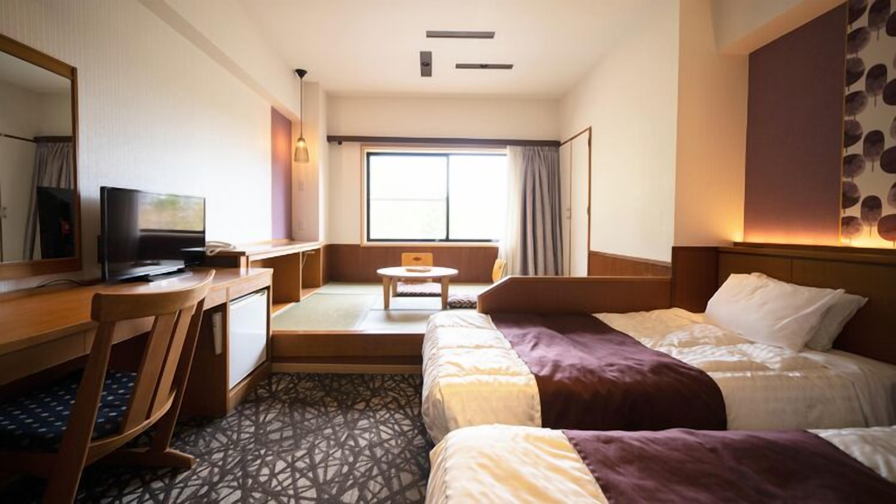 Una habitación de hotel con cama, escritorio, televisor y ventana con cortinas.