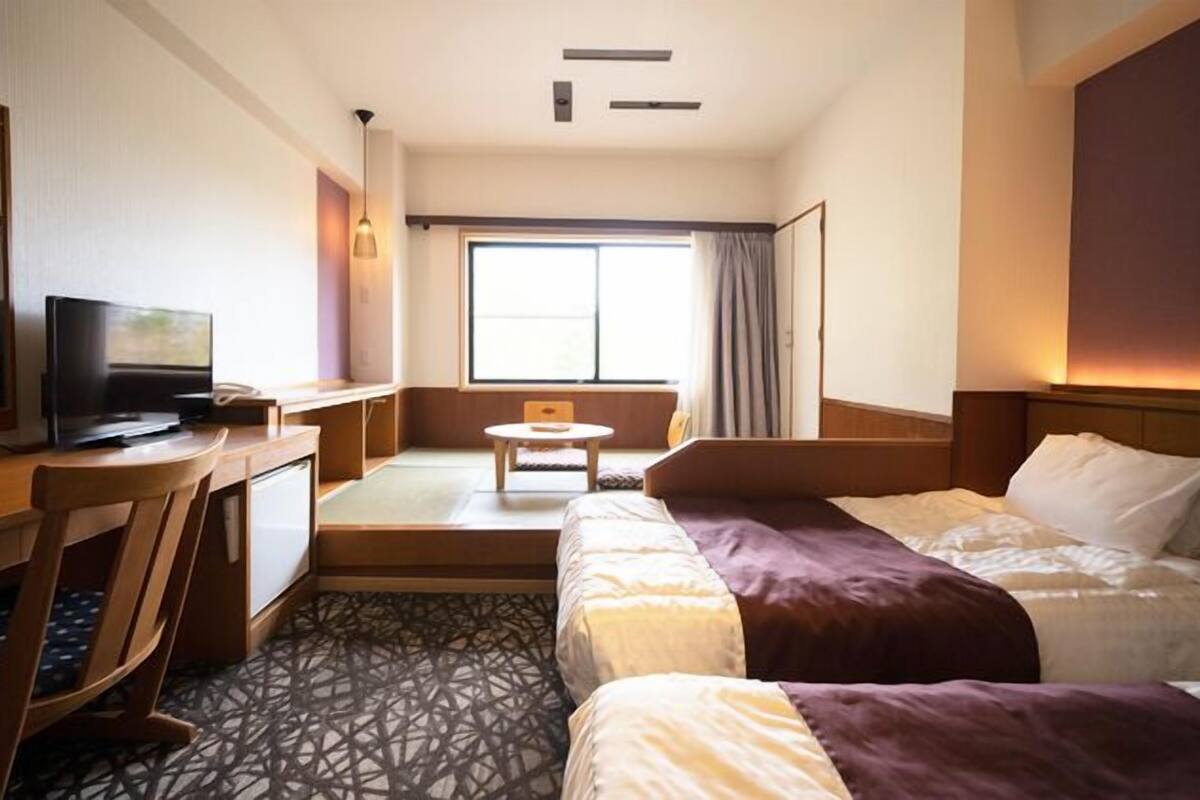 A hotel room with a bed, a desk, a television, and a window with curtains.