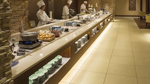 Een lange buffetlijn met koks die eten bereiden, een stenen muur en een betegelde vloer.
