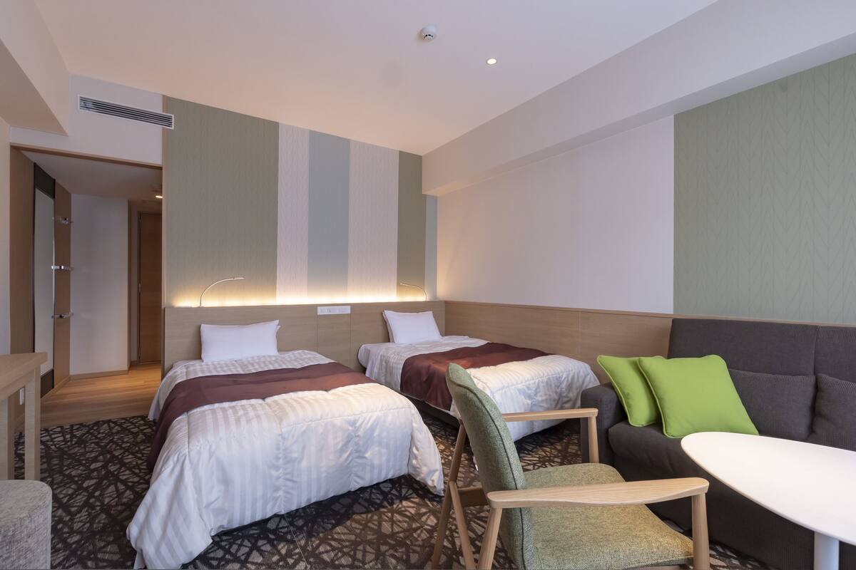 A hotel room with two beds, a sofa, a small table, and a chair.