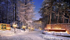 Een sneeuwbedekte pad dat leidt naar de ingang van een hotel, met verlichte borden en een bakstenen muur.