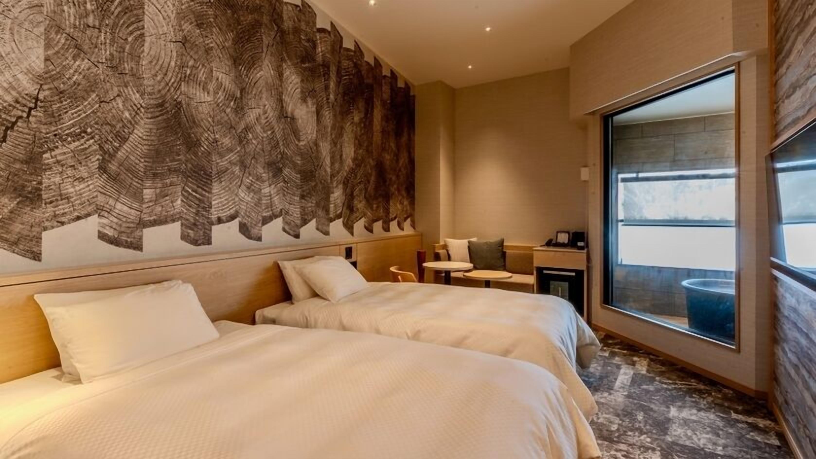 A hotel room with two beds, a small table, a chair, and a large window.