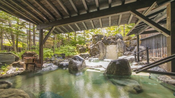 Een traditioneel Japans onsen met een houten constructie, rotsformaties en een heldere warmwaterbron.