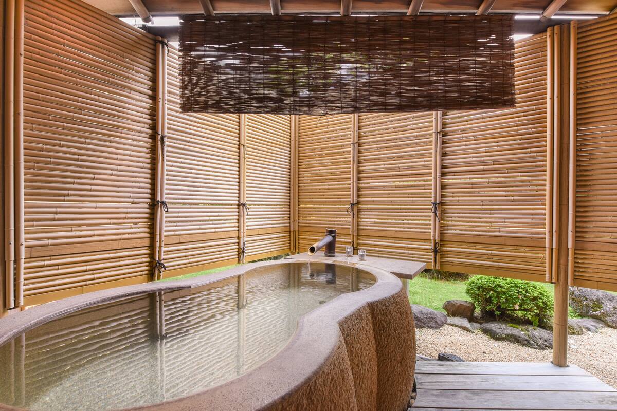 A hot spring bath area with a wooden enclosure, a stone basin, and a small garden with rocks and greenery.