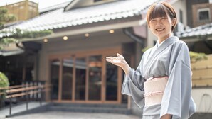 A person in traditional attire standing in front of a building with a tiled roof and a glass entrance. - Furuya Ryokan (Atami)