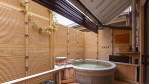 A traditional Japanese onsen with a stone hot spring, wooden deck, bamboo walls, and a wooden bench. - Furuya Ryokan (Atami)