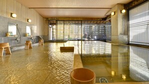 A traditional Japanese onsen with wooden benches, a large hot spring pool, and a view of the outside through large sliding doors. - Furuya Ryokan (Atami)