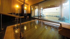 A hot spring bath with wooden railings and a view of a building through large glass doors. - Furuya Ryokan (Atami)