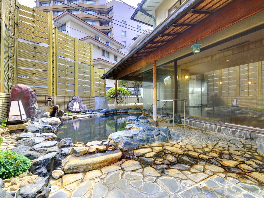 En traditionel japansk onsen med et stenbadekar omgivet af sten og et træhegn.