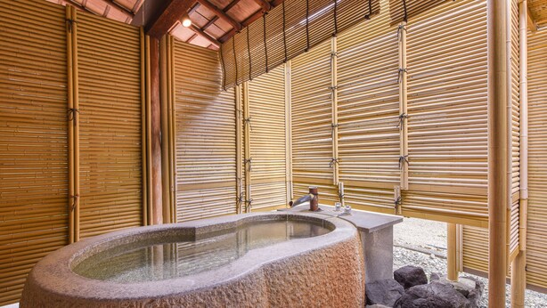 A stone hot tub in a room with bamboo walls and a tiled floor. - Furuya Ryokan (Atami)
