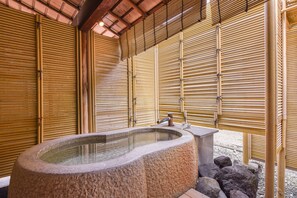 A stone hot tub in a room with bamboo walls and a tiled floor. - Furuya Ryokan (Atami)