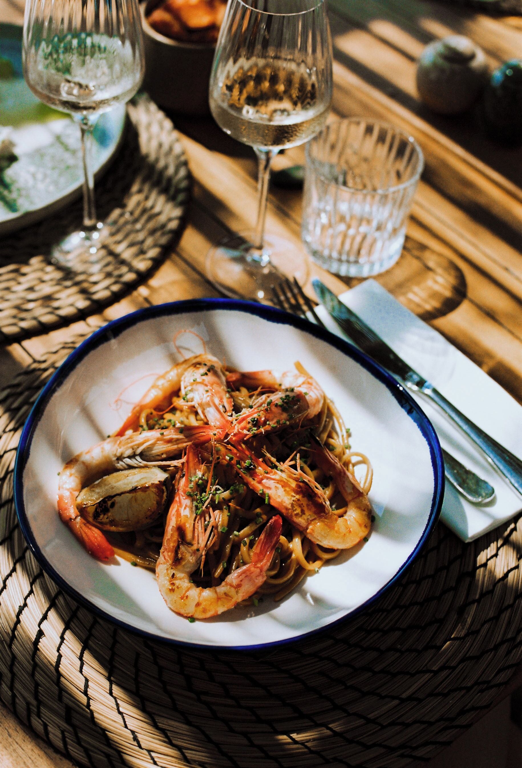 A plate of seafood pasta with a fork and knife on a woven placemat.