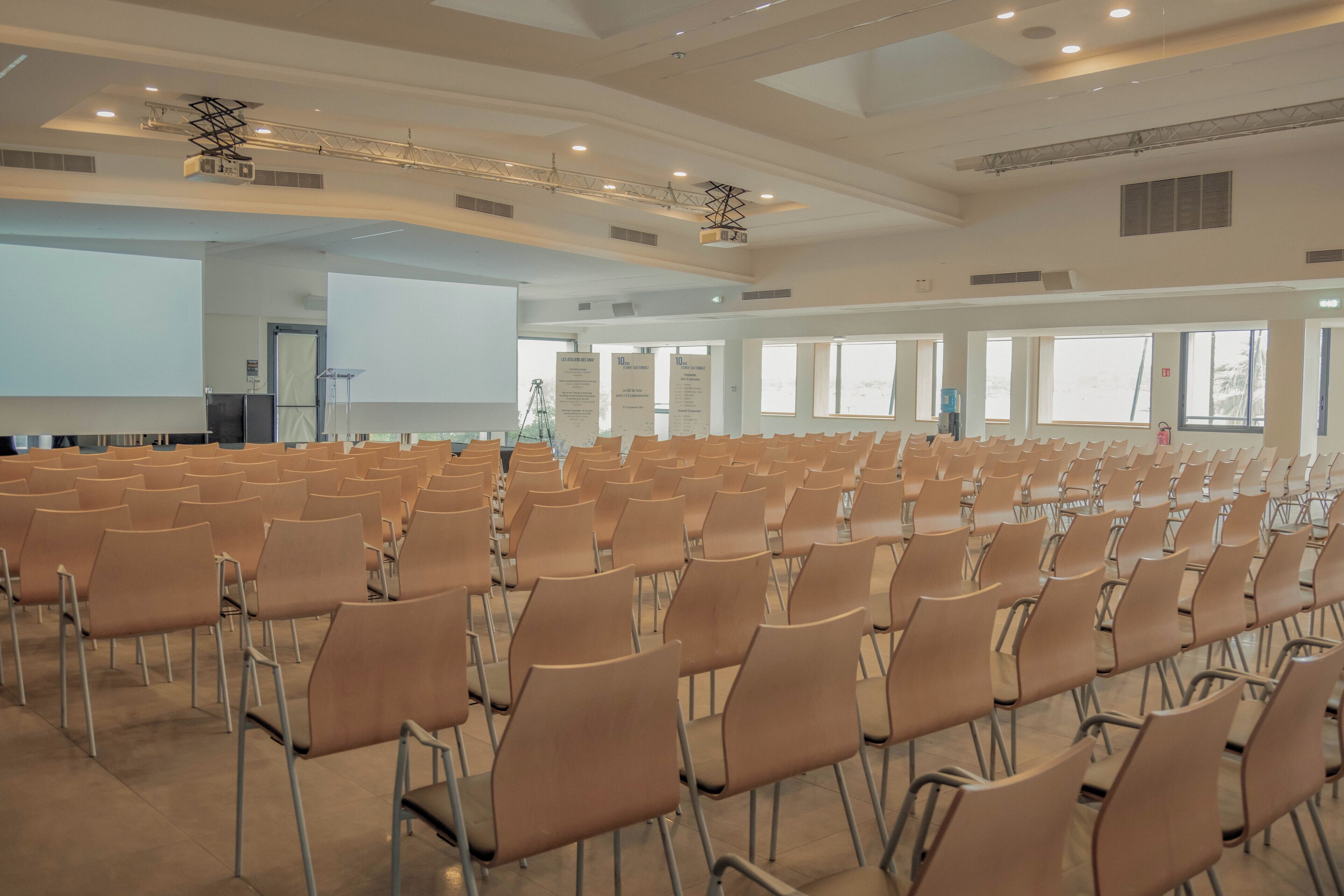 Ein großer Konferenzraum mit Reihen von Stühlen, einer Projektionsleinwand und einer Bühne mit einem Rednerpult.