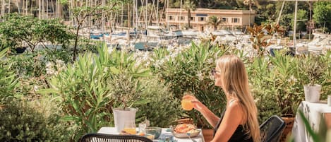 A dining table with a view of a marina and boats, surrounded by potted plants.