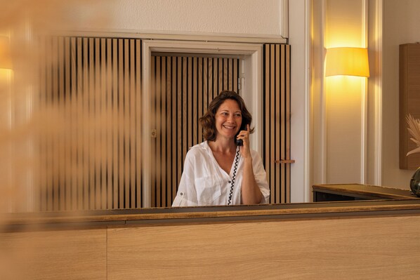 A reception desk with a wooden finish and a mirror reflecting a person holding a phone.