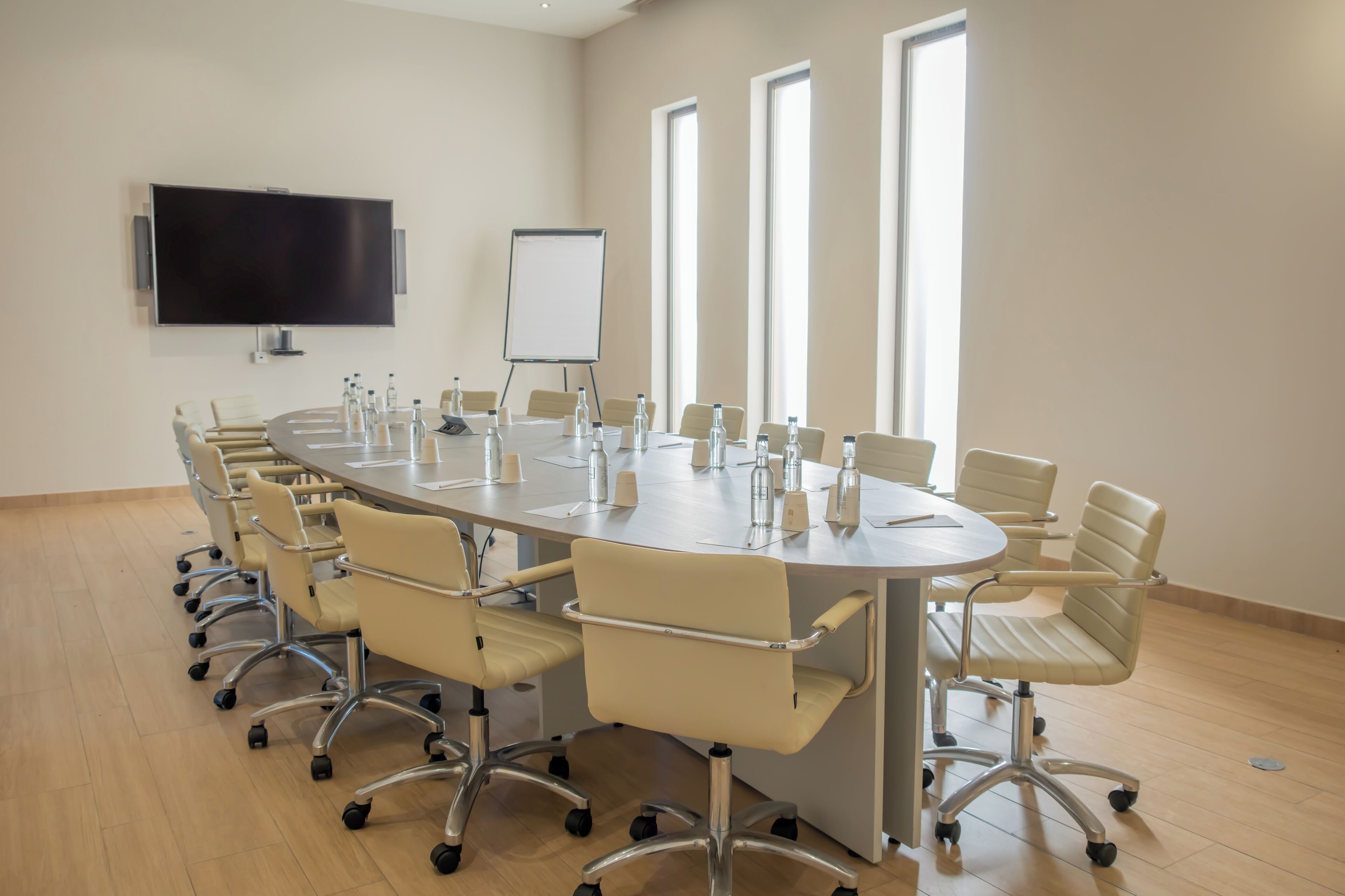 Une salle de conférence équipée d’une grande table, de chaises, d’un tableau blanc et d’un téléviseur.