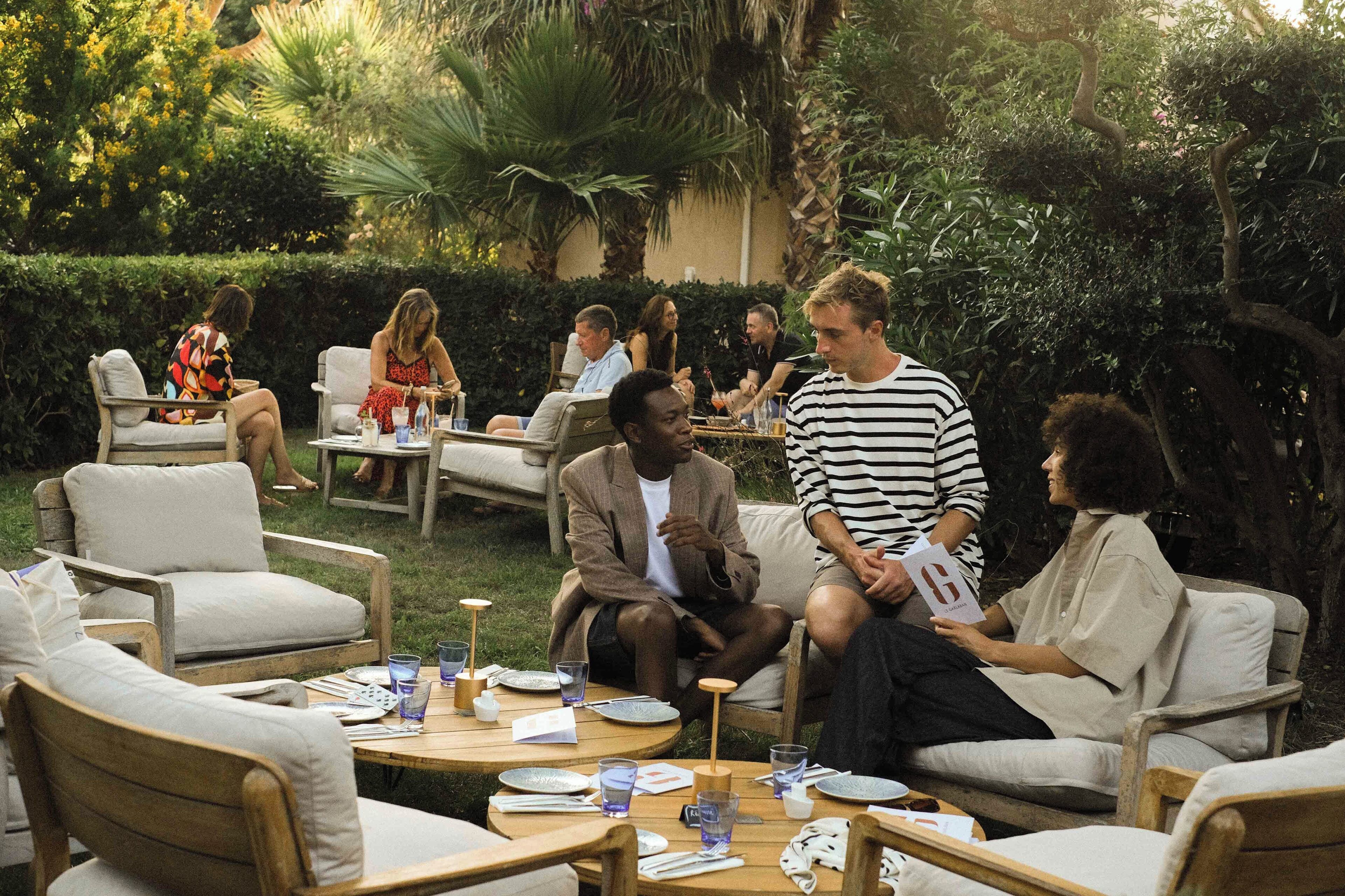 An outdoor seating area with round tables and chairs, surrounded by lush greenery and palm trees.