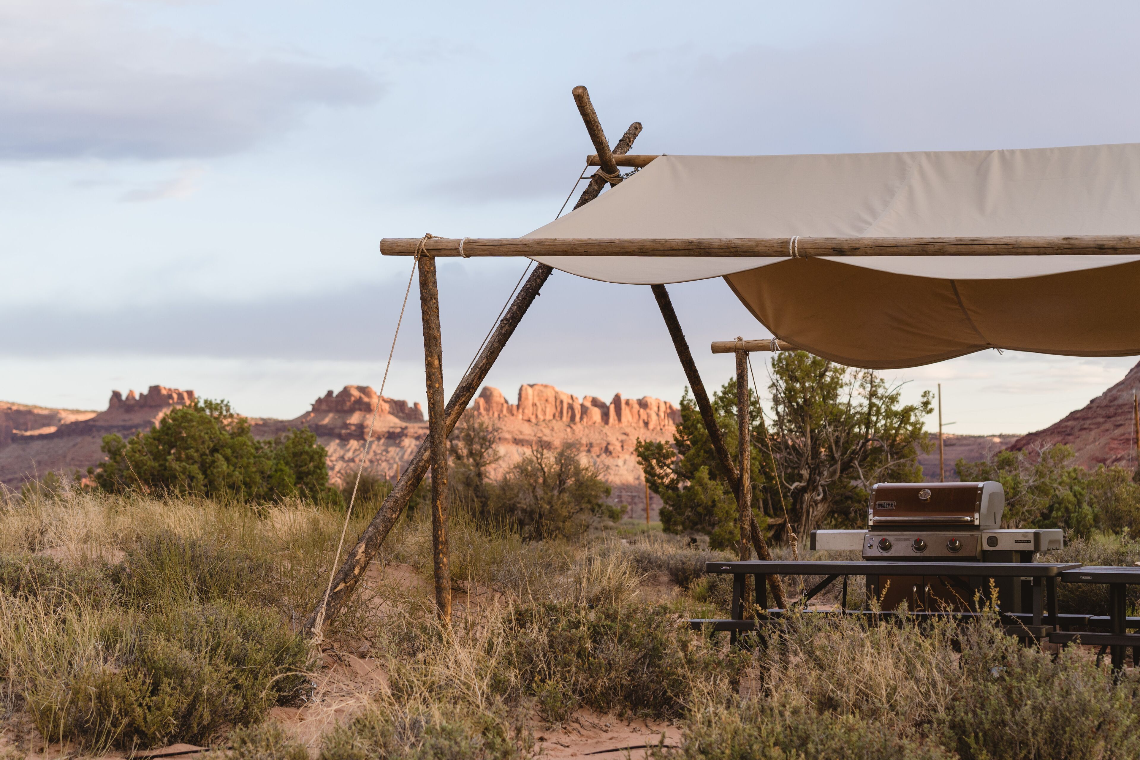 A camping setup with a tent, a grill, and a picnic table in a natural landscape.