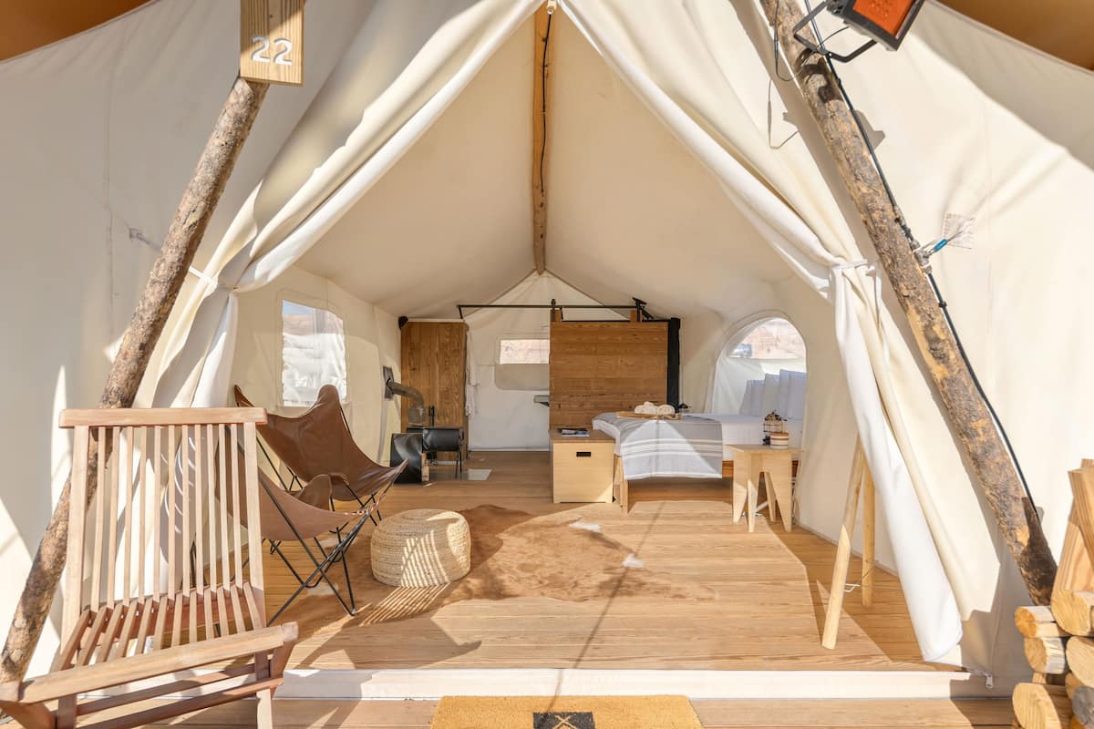A tent with a bed, a chair, a small table, and a wooden bench.