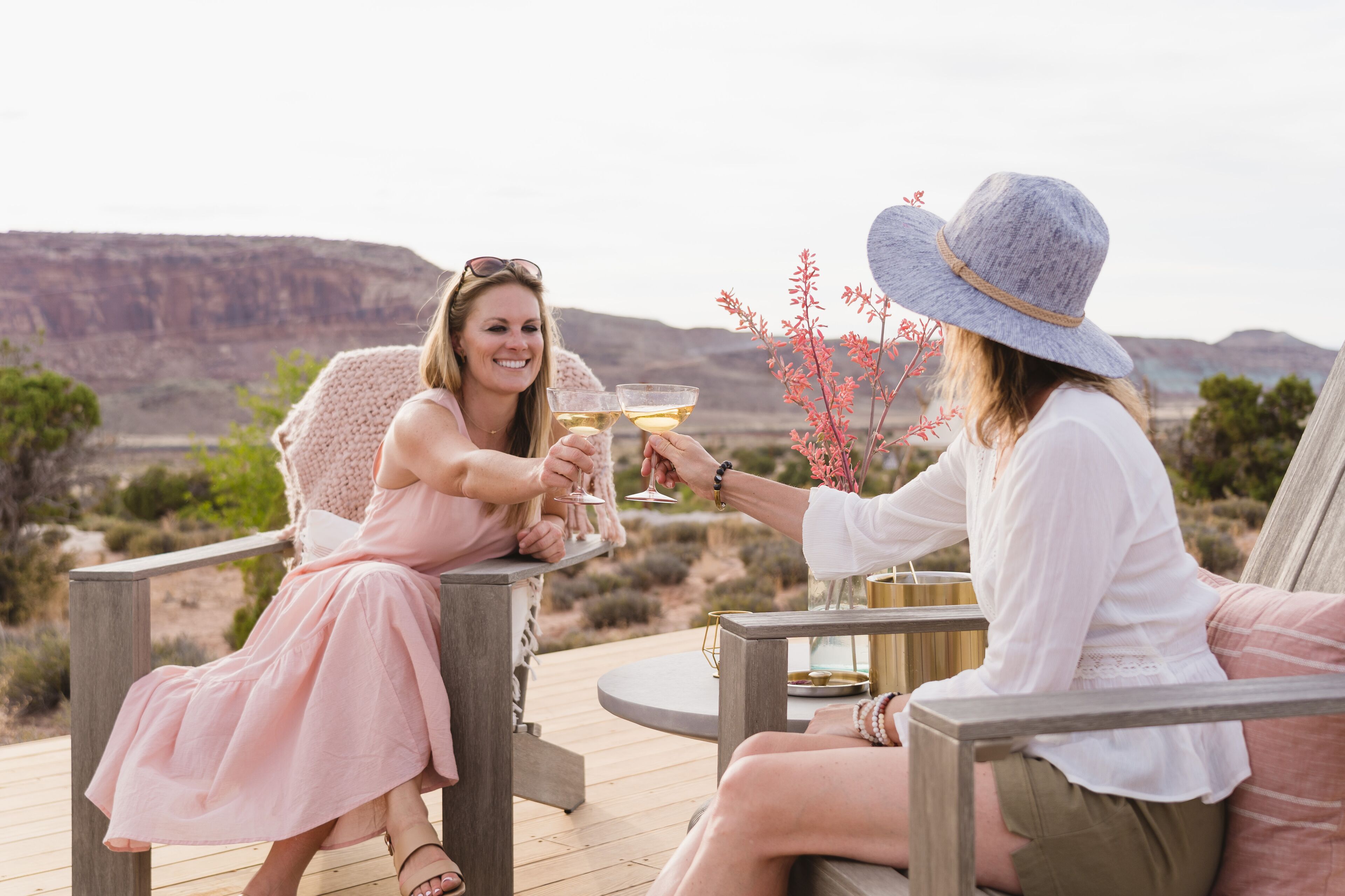 Two people toasting with drinks on an outdoor deck with a mountainous backdrop.