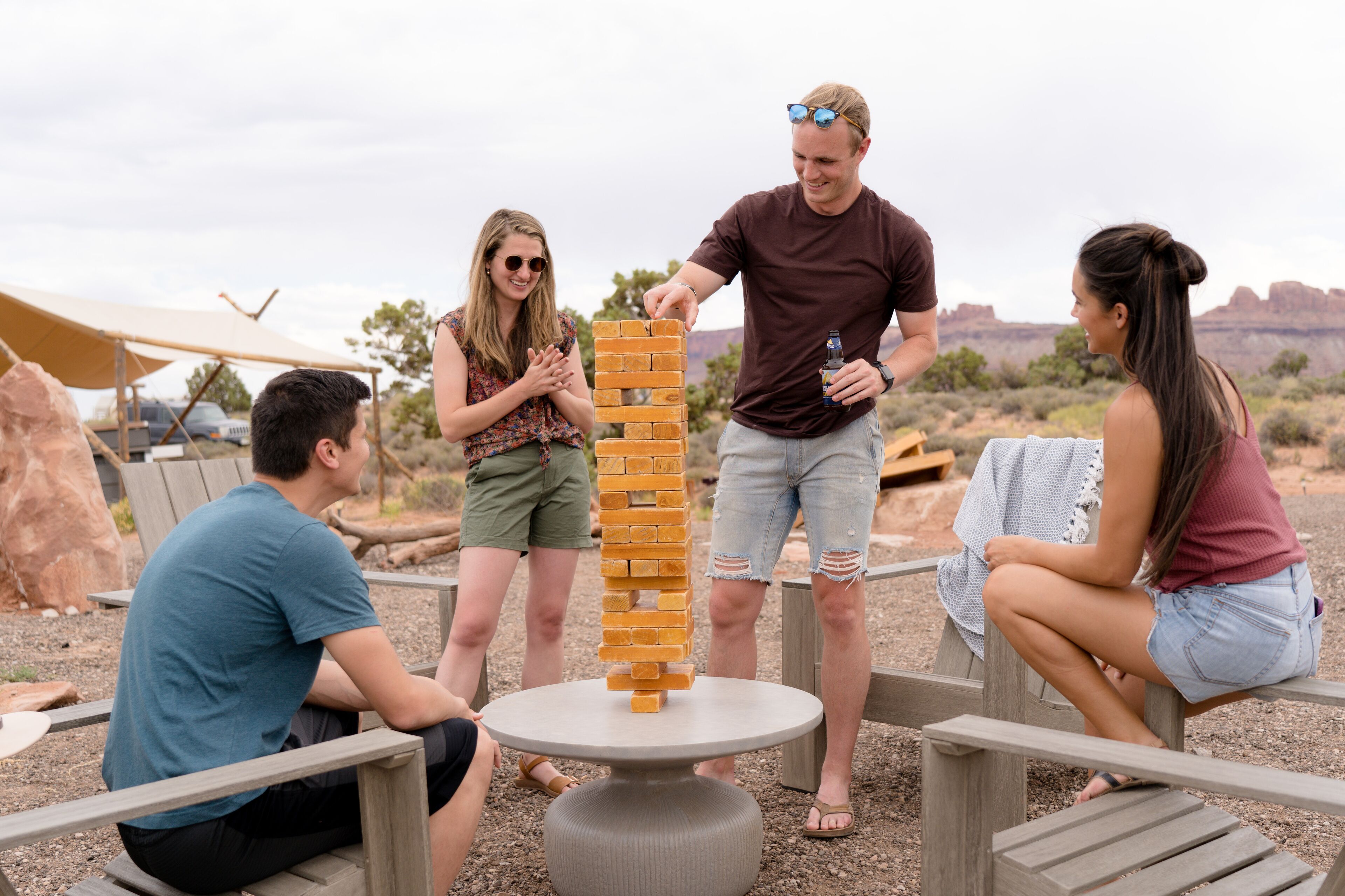 A group of people playing a game of Jenga at an outdoor setting with a round table and wooden benches.