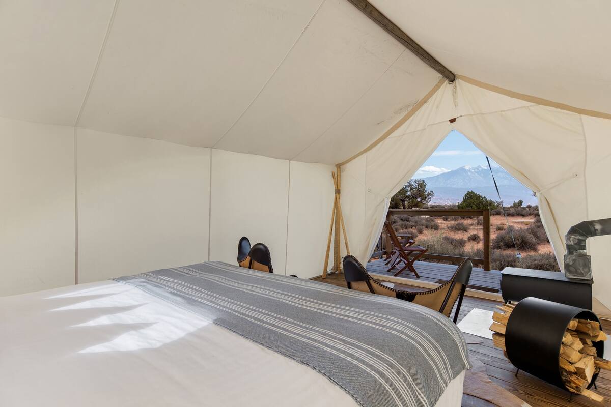 A tented accommodation with a bed, chairs, and a wood stove.