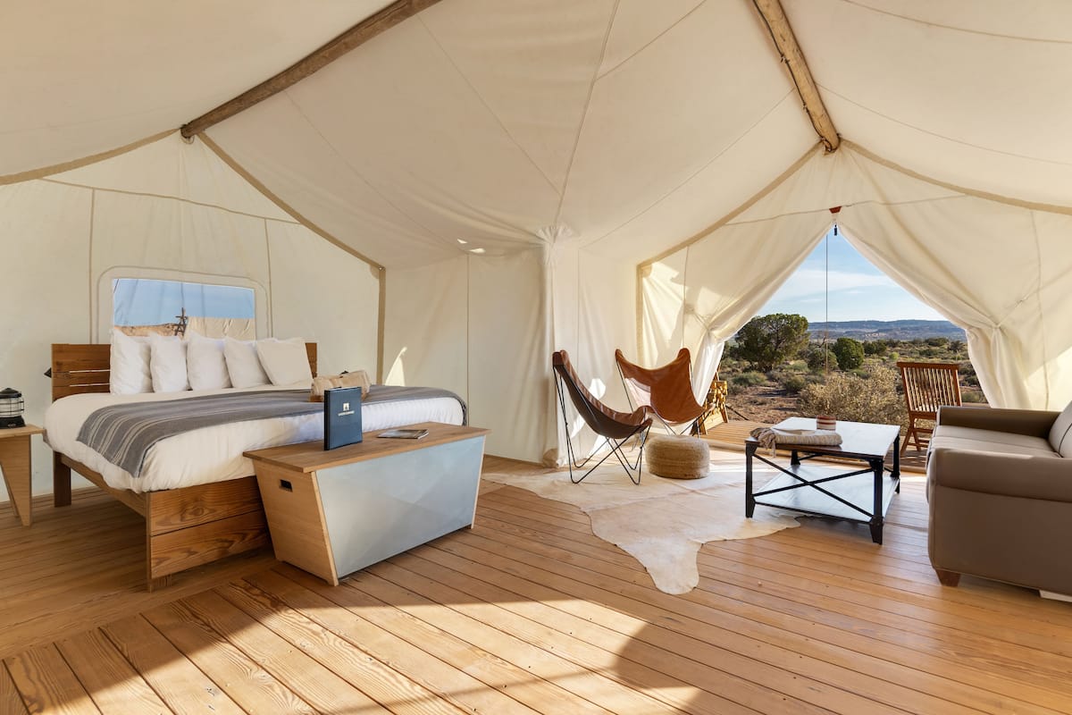 A tented accommodation with a bed, wooden furniture, and a view of the landscape.