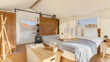 A spacious tented room with a large bed, wooden flooring, and a view of the outdoors.